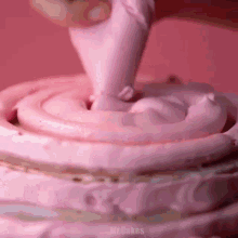 a close up of a person frosting a cake with pink frosting .
