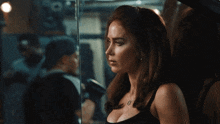 a woman in a black tank top stands in front of a glass door