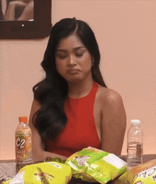 a woman in a red top sits at a table with chips and a bottle of c2 breeze