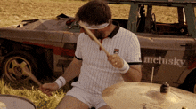 a man playing drums in front of a car that says melusky