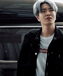 a young man wearing a black jacket and a white supreme shirt
