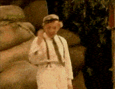 a man wearing suspenders and a hat is standing in front of a large rock
