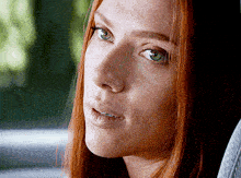 a woman with red hair and green eyes looks at the camera