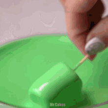 a person is dipping a green marshmallow into a green bowl