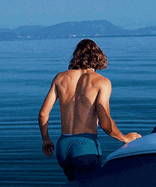a shirtless man in blue shorts is standing in the water near a boat