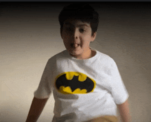 a young boy wearing a white batman t-shirt is making a funny face