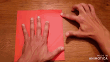 a person 's hands folding a piece of red paper with the words made in animatica below them