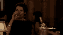 a woman in a black dress is drinking a glass of wine .