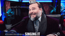a man with a beard is sitting in front of a microphone with the words crit singing it above him
