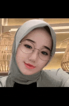 a woman wearing a hijab and glasses is smiling for the camera