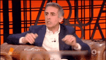 a man in a suit is sitting on a couch and talking on a show called the cityman