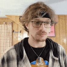 a man wearing glasses and a bandana with the letter t on it looks at the camera