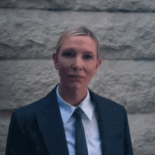 a woman in a suit and tie is standing in front of a wall .