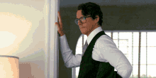 a man wearing glasses and a vest leans against a door