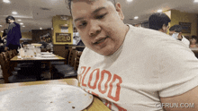 a man wearing a t-shirt that says blood is sitting at a table with a pizza in front of him