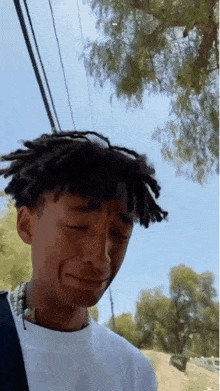 a young man with dreadlocks is crying while wearing sunglasses and a necklace .