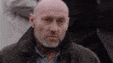 a bald man with a beard wears a black jacket