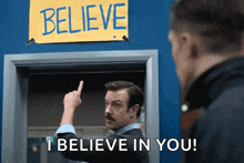 a man standing in front of a sign that says believe i believe in you
