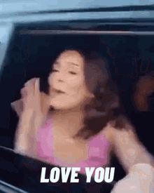 a woman in a pink tank top is sitting in a car and says love you
