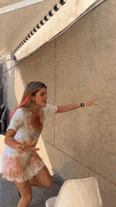 a woman in a bloody dress is standing in front of a wall and a chair .