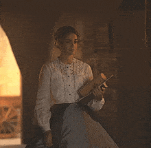 a woman in a white shirt and black skirt is holding a book in her hands .