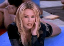 a woman laying on her stomach with her hand on her face and a man in the background