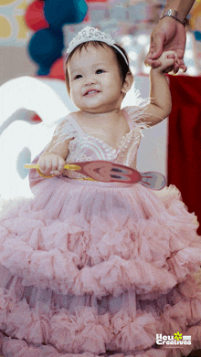 a little girl wearing a pink dress and a tiara holds a candy cane