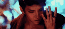 a young man with a ring on his finger is covering his face with his hands .