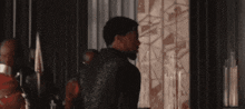 a man in a black jacket is standing in front of a wall in a dark room .