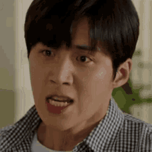 a young man in a plaid shirt is making a funny face with his mouth open .