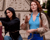 two women are standing next to each other and one is wearing a blue shirt and a tan jacket