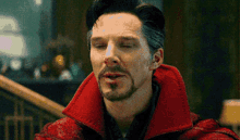 a man with a beard and mustache is wearing a red coat and making a funny face with his eyes closed .