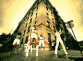 a group of women are dancing on a street in front of a building with a sign that says one way