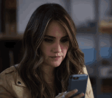 a woman in a tan jacket looks at her cell phone