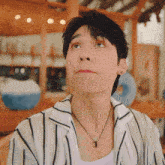a man wearing a striped shirt and a necklace looks up at something