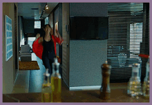 a woman in a red jacket is walking down a hallway in front of a television
