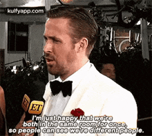 a man in a tuxedo is talking into a microphone while standing in front of a crowd .