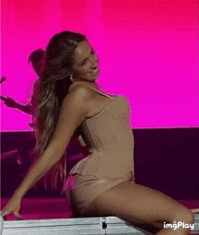 a woman in a corset is sitting on a table with a pink background and the word imgplay at the bottom right
