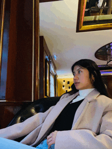 a woman in a pink coat sits on a black leather chair