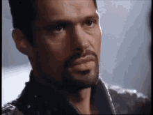 a close up of a man 's face with a beard and a leather jacket .