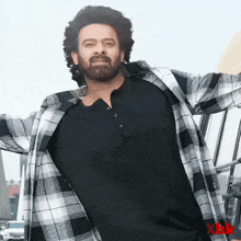 a man with a beard wearing a black shirt and a plaid shirt with the letter x on the bottom
