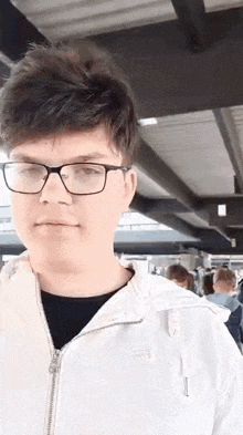 a young man wearing glasses and a white jacket is standing in a crowd of people .