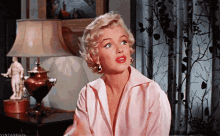 a woman in a pink shirt is sitting in front of a lamp .