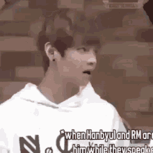 a young man wearing a white hoodie with the words when hanbyul and rm are him while they speak .