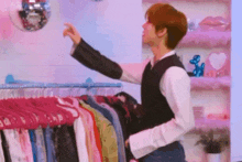 a man is standing in front of a rack of clothes and pointing at a mirror .