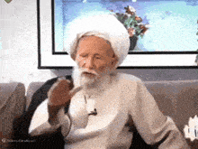 a man with a beard wearing a white turban is sitting on a couch smoking a pipe