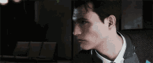 a man in a suit and tie is sitting in a dark room looking at something .