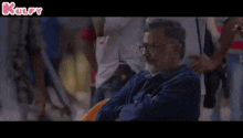 a man wearing glasses is sitting in a chair in a crowd of people .