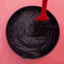 a red spatula is being used to stir a black liquid