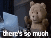 a teddy bear is sitting at a table in front of a laptop computer .